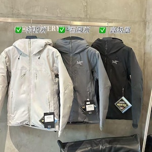 Może przedstawiać: Trzy kurtki z kapturem w kolorze jasnoszarym, szarym i czarnym wiszą na wieszaku. Każda kurtka ma zapięcie na zamek błyskawiczny, kieszenie i logo na piersi. Do każdej kurtki przymocowane są metki. Tekst nad kurtkami jest po chińsku.