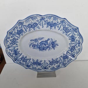 Op de afbeelding: Ovale keramische schaal met een geschulpte rand, met een blauw-wit bloemmotief. Het midden toont een blauw konijn te midden van bloemen. De rand is versierd met een herhalend bloemmotief.