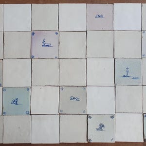 Pode incluir: Uma coleção de trinta e cinco azulejos de cerâmica quadrados dispostos em uma grade. Os azulejos são principalmente brancos, alguns com tons de azul claro ou cinza. Vários azulejos exibem pequenas ilustrações detalhadas em tinta azul.
