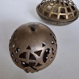 Peut inclure: Deux sphères décoratives antiques en métal. L'une est une sphère complète avec des formes géométriques découpées. L'autre est une demi-sphère avec un motif en treillis. Les deux ont un aspect vieilli et terni, suggérant qu'il s'agit d'objets vintage.