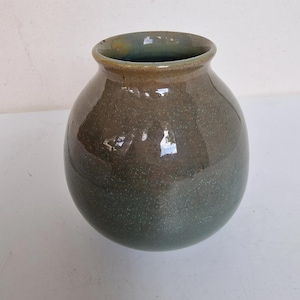 Può includere: Un vaso in ceramica fatto a mano con un corpo arrotondato e un bordo leggermente svasato. Il vaso presenta una sfumatura di colore, che passa da un verde scuro maculato alla base a un verde oliva più chiaro nella parte superiore. La superficie ha una finitura lucida.