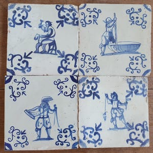 Op de afbeelding: Vier vierkante keramische tegels met blauw-witte ontwerpen. Elke tegel heeft een andere illustratie van een persoon in een historisch kostuum, met decoratieve blauwe krullen aan de randen. De tegels zijn samen gerangschikt en tonen een samenhangend ontwerp.