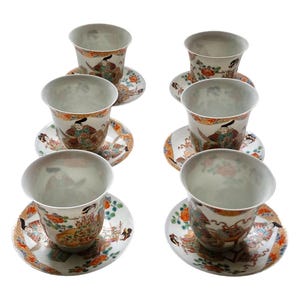 May include: Six porcelain teacups and saucers. The cups and saucers feature a detailed, colorful design with figures, flowers, and ornate patterns. The cups are white inside and have a flared rim. The saucers are round and decorated with similar motifs.