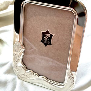 Peut inclure: Un cadre photo rectangulaire en argent sterling avec une finition polie et des coins arrondis. Le cadre présente des motifs en relief de coquillages et de vagues sur le côté gauche. Un insert en velours beige porte une étiquette PLATA 925.