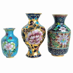 May include: Three decorative cloisonné vases with floral designs. The vases feature a variety of colors, including blue, gold, pink, and green. The vases are of different sizes and shapes, with intricate detailing.