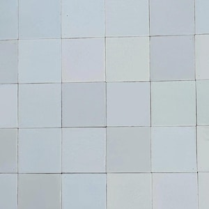Puede incluir: Una cuadrícula de baldosas cuadradas de color blanquecino. Las baldosas están dispuestas en un patrón uniforme, con líneas oscuras de lechada que separan cada baldosa. Las baldosas tienen una superficie ligeramente texturizada y el color varía ligeramente.