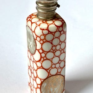 Op de afbeelding: Een rechthoekige keramische fles met een witte basis en een patroon van onderling verbonden oranje cirkels. De fles bevat twee ronde inzetstukken met een houtnerftextuur en is afgesloten met een zilverkleurige metalen schroefdop.