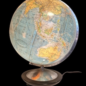 Puede incluir: Un globo terráqueo antiguo con un mapa del mundo detallado, que muestra los países en varios colores. El globo está montado sobre un soporte de metal oscuro con una base circular y un asa. El fondo es negro.
