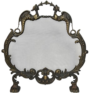 May include: A brass fireplace screen featuring a fine metal mesh centre framed by ornate scrollwork. The top of the frame displays two dragon figures facing each other, while the base is supported by two feet shaped like animal paws.