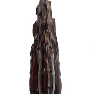 Op de afbeelding: Een donkerbruin, gebeeldhouwd houten beeld met een verticaal, abstract ontwerp. De sculptuur heeft een gladde, gepolijste afwerking en heeft een gezichtachtige vorm aan de onderkant. De houtnerf is zichtbaar en voegt textuur toe aan het stuk.