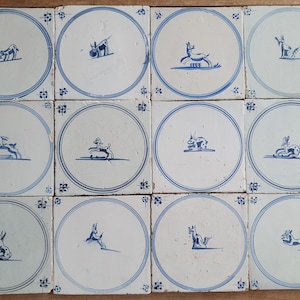 Puede incluir: Un conjunto de doce azulejos de cerámica cuadrados dispuestos en una cuadrícula. Cada azulejo de color blanco roto presenta un borde circular azul con motivos florales en las esquinas y una ilustración central azul pintada a mano.