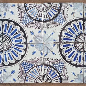 Könnte beinhalten: Acht quadratische Keramikfliesen mit einem sich wiederholenden Muster. Jede Fliese zeigt ein zentrales blau-weißes Blumendesign mit schwarzem Rand. Die Fliesen sind in zwei Reihen zu je vier Stück angeordnet, für dekorative Zwecke.