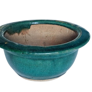 Op de afbeelding: Een teal-kleurige keramische kom met een brede, licht uitlopende rand. De kom heeft een glanzende afwerking met zichtbare craquelé, en de binnenkant is een contrasterende bruine kleur. Het ontwerp is eenvoudig en functioneel.