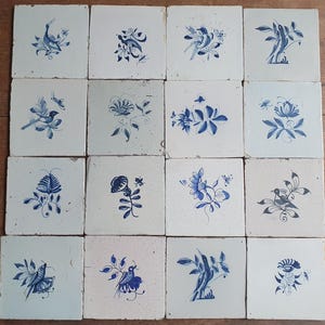 May include: A collection of sixteen square ceramic tiles arranged in a four-by-four grid. Each off-white tile features a unique hand-painted blue illustration of various birds, flowers, and foliage, showcasing intricate line work and details.