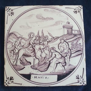 Może przedstawiać: Kwadratowa płytka ceramiczna z fioletową ilustracją wewnątrz kolistej ramki. Scena przedstawia postać jadącą na osiołku, otoczoną przez kilka osób, z budynkiem w tle. Na dole nadrukowany jest tekst MAT. 21.