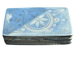 Puede incluir: Una caja rectangular de metal plateado con un intrincado diseño grabado en la tapa. El centro muestra un gran motivo de estrella rodeado por un borde circular, con patrones florales más pequeños y líneas radiantes en las esquinas.