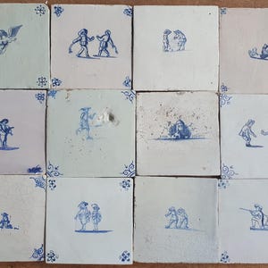 Puede incluir: Una colección de doce azulejos de cerámica cuadrados dispuestos en cuadrícula. Cada azulejo de color blanco roto presenta ilustraciones azules pintadas a mano de figuras, paisajes o un ángel, con motivos decorativos azules en las esquinas.