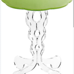 May include: A modern accent table with a clear acrylic base and a light green, leaf-shaped top. The table's base features a decorative, flowing design. The table is approximately 20 inches tall.