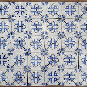 Puede incluir: Conjunto de baldosas cerámicas cuadradas con fondo blanco y diseño floral azul. Las baldosas están dispuestas en un patrón de cuadrícula, mostrando un diseño repetitivo de flores y hojas estilizadas. Las baldosas son probablemente para uso decorativo o funcional.