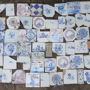 Puede incluir: Una colección de azulejos de cerámica variados con diseños pintados a mano en azul y blanco, que incluyen motivos florales, paisajes, formas geométricas y texto. Los azulejos varían en forma y tamaño, mostrando signos de antigüedad y desgaste.