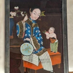 Può includere: Dipinto antico incorniciato raffigurante una donna in abito blu con dettagli dorati, che tiene un ventaglio. Un bambino le offre una pesca. L'opera presenta uno sfondo scuro e una cornice decorativa, arte asiatica tradizionale.