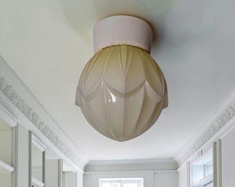 May include: A ceiling-mounted light fixture featuring a spherical, cream-colored glass shade with a molded, petal-like pattern. The fixture includes a cylindrical, pale-colored base that attaches directly to the ceiling surface.