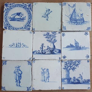 以下が含まれることがあります： 白い背景に青い手描きのイラストが施された、9枚の正方形のセラミックタイルがグリッド状に並んでいます。デザインには、犬、走る人物、帆船、馬、木の下の人々、風景などが描かれています。