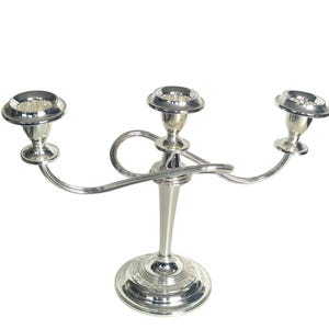 Puede incluir: Un candelabro de metal plateado con tres portavelas dispuestos en brazos curvos. El vástago central se eleva desde una base circular escalonada con cuentas decorativas. Cada copa para vela tiene un borde ancho y plano con textura.