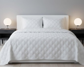 May include: A white bed with a matching quilted comforter and two pillows. Two black nightstands flank the bed, each with a round, white lamp. The bed is centered against a gray wall.