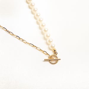 May include: A delicate necklace featuring a strand of creamy white pearls and a gold-colored chain. The necklace is secured with a gold-colored toggle clasp. The jewelry is displayed on a white background.