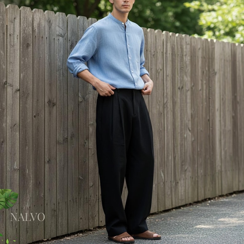 May include: A light blue long-sleeve shirt with a mandarin collar and black pleated trousers. The outfit is completed with brown sandals. The clothing is worn near a wooden fence.