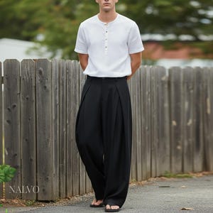 May include: A person wearing a white short-sleeved shirt with a button-up collar and black wide-leg pants. The pants have pleats at the waist. The image is taken outdoors near a wooden fence.