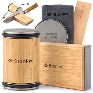 Op de afbeelding: Een verzameling messenslijpgereedschap. De set bevat een cilindrische bamboe messenslijper, een rechthoekig bamboe slijpblok, een diamanten slijpsteen, een grijze microvezeldoek en een leren strop. De merknaam "Stonka" is zichtbaar.