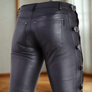 May include: Black leather pants with a classic five-pocket design. The pants feature decorative buckles on the side and are made of a smooth, shiny material. The back pockets have small, silver rivets.