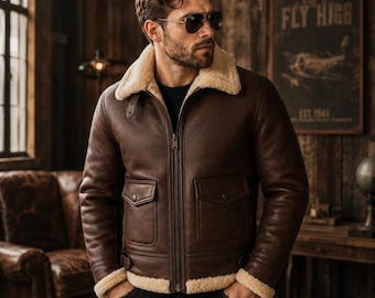 Può includere: Un giubbotto bomber in pelle marrone scuro con un colletto spesso in montone color crema e polsini abbinati. La giacca presenta una chiusura centrale con zip in metallo, due tasche frontali con patta e bottoni a pressione e cinturini laterali.
