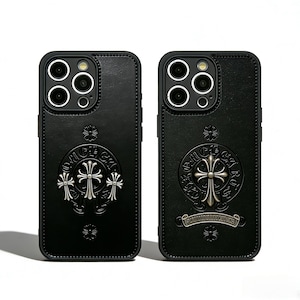 May include: Two black leather phone cases with silver cross designs. The cases have a textured appearance and feature a decorative cross emblem. The phone cases are designed to fit a phone with multiple camera lenses.