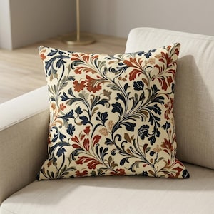 May include: A square throw pillow featuring a cream-colored background with a dense, repeating botanical pattern. The design consists of swirling acanthus-style leaves and floral motifs in deep navy blue, burnt orange, and muted sage green tones.