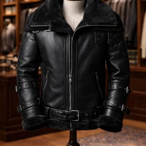 May include: A black leather jacket with a shearling collar and lining, displayed on a mannequin. The jacket features a zip-up front, multiple buckles, and a belt. The text "Urban Hide Fashion" is visible at the bottom.
