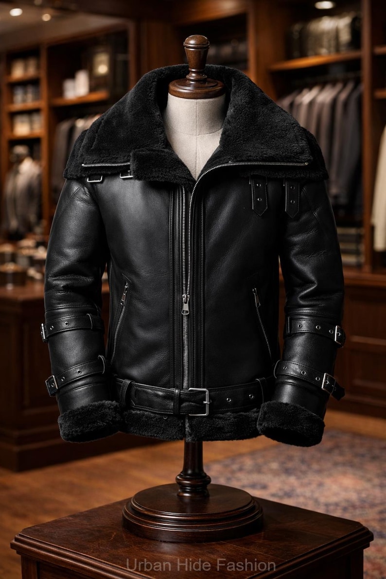 May include: A black leather jacket with a shearling collar and lining, displayed on a mannequin. The jacket features a zip-up front, multiple buckles, and a belt. The text "Urban Hide Fashion" is visible at the bottom.