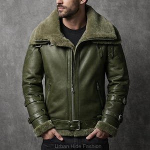 May include: An olive green leather jacket with a shearling collar and lining. The jacket has a front zip, multiple pockets, and adjustable straps on the sleeves and waist. The text "Urban Hide Fashion" is visible at the bottom.
