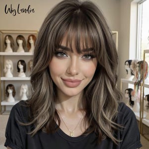 Puede incluir: Una peluca de longitud hasta los hombros con cabello castaño ondulado y en capas, con reflejos más claros y flequillo despuntado. El cabello tiene una apariencia suave y texturizada con volumen en la coronilla y los lados. Texto Wig Landia.
