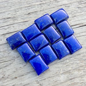 Può includere: Una collezione di gemme rettangolari di lapislazzuli lucidati. Le pietre blu scuro, con macchie dorate, sono disposte su una superficie di legno invecchiato. Queste gemme sono ideali per la creazione di gioielli.