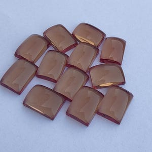 Può includere: Undici piastrelle di vetro color ambra, rettangolari con angoli arrotondati. Ogni piastrella ha una superficie leggermente curva e bordi marrone-rossastro. Le piastrelle sono disposte su una superficie bianca. Ogni piastrella misura circa 2 cm.