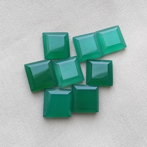 Può includere: Una collezione di sette pietre preziose verdi a taglio quadrato con superfici sfaccettate. Ogni pietra presenta una parte superiore piatta e bordi smussati, mostrando una tonalità verde smeraldo uniforme e una finitura lucida e riflettente.