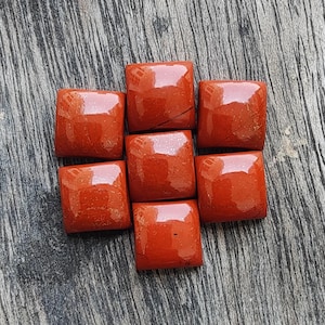 May include: Seven square-shaped red jasper cabochons with a polished, glossy finish. Each stone features a smooth, slightly domed surface with natural variations in the deep red color and subtle dark veining visible across the flat, square faces.