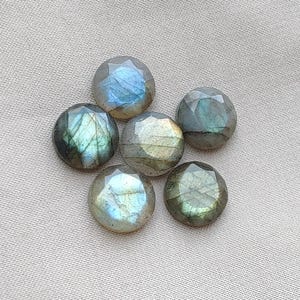 May include: Five round, faceted labradorite gemstones arranged in a cluster. Each stone displays a unique iridescent sheen with flashes of blue, green, and gold light reflecting across the polished, geometric surfaces of the cut mineral cabochons.