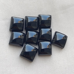 May include: A collection of eight small, square-shaped black cabochons with a smooth, polished, and reflective surface. Each piece features a slightly domed top and sharp, defined edges, creating a uniform appearance across the entire set of stones.