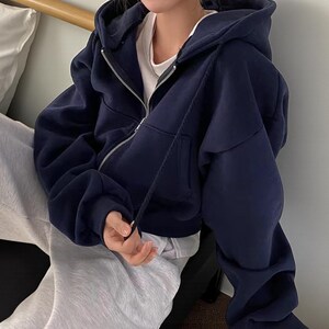 Op de afbeelding: Een marineblauwe hoodie met ritssluiting, capuchon met trekkoord en voorzakken. De hoodie is gemaakt van een zacht, dik materiaal en heeft een zilveren rits. De mouwen zijn lang en de pasvorm is relaxed.