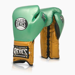 Peut inclure: Une paire de gants de boxe vert métallisé et doré avec des lacets noirs. Les gants présentent le logo Cleto Reyes en noir et blanc sur le poignet et le dos de la main, avec le logo WBC imprimé sur le côté au niveau de la zone du pouce.