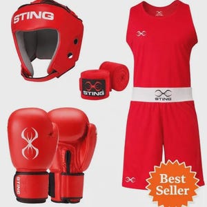 Op de afbeelding: Een rode boksset bestaande uit een hoofdbeschermer, een paar bokshandschoenen, handwindsels en een mouwloos shirt met bijpassende broek. De items zijn voorzien van het Sting-logo. De tekst in de afbeelding luidt Red Boxing Set, Boxing Gloves, Headguard, Outfit & Wraps en Best Seller.
